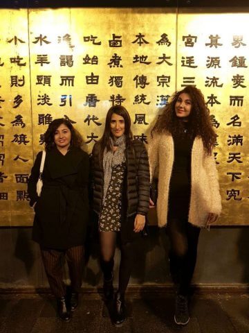 Enza with two friends in front of a wall covered in Chinese characters